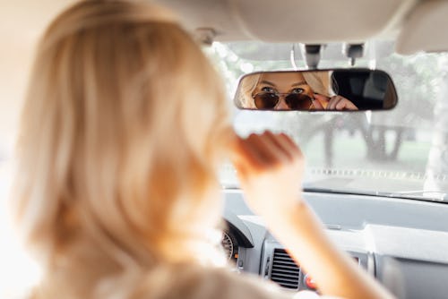 A woman adjusts her sunglasses in the rearview mirror of her car. These 3 zodiac signs will be most ...