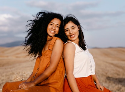 two young women with their backs towards each other smile as they chat about aries-taurus compatibil...