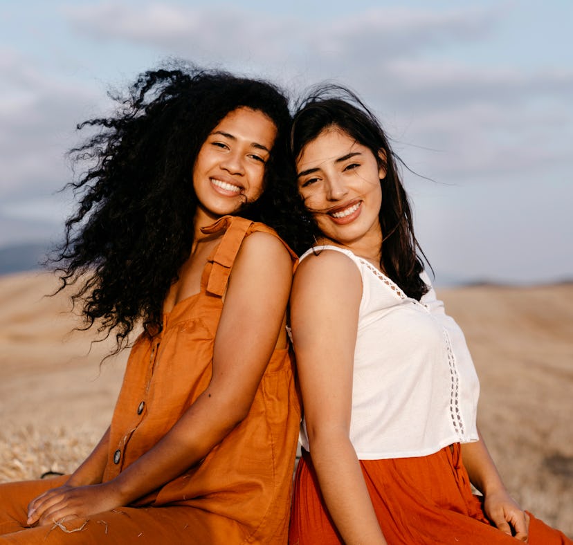 two young women with their backs towards each other smile as they chat about aries-taurus compatibil...