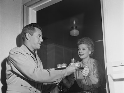 American actress Lucille Ball (1911 - 1989) passing a coffee tray to her husband, actor and musician...
