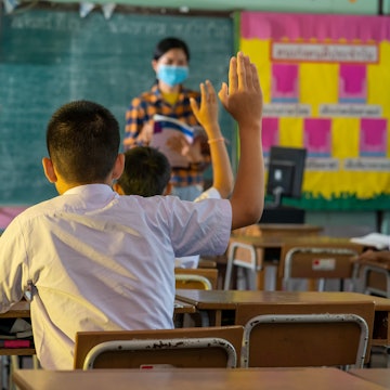 A child raises their hand in a sparse classroom. Schools across the country have seen an uptick in c...