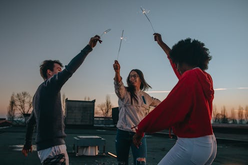Young friends dancing and having fun while holding burning sparklers on roof during dusk