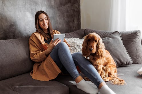 Smiling woman resting with her dog and reading magazine on digital tablet