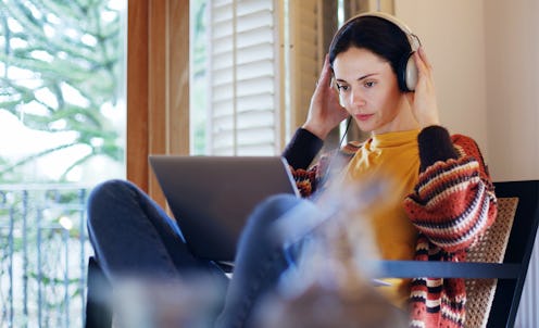 Stock image of a dark-haired young woman reclining at home with her laptop & headphones, she’s work...