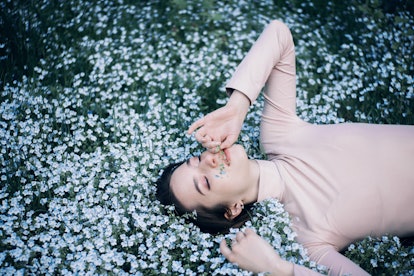 Young woman laying in a field of daisies during the week of of March 14, 2022, the best week for her...