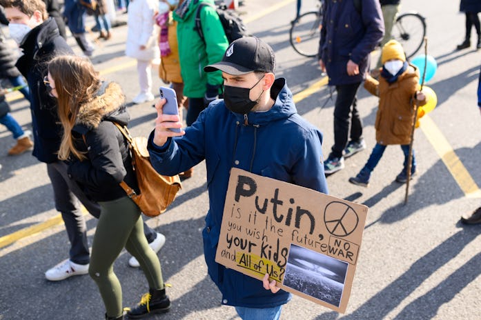 05 March 2022, Hamburg: A demonstrator with a placard films with his smartphone. Supported by numero...