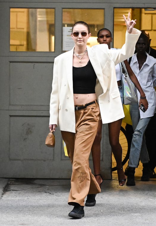 NEW YORK, NEW YORK - JUNE 28: Gigi Hadid is seen wearing a white blazer, black crop top, brown pants...