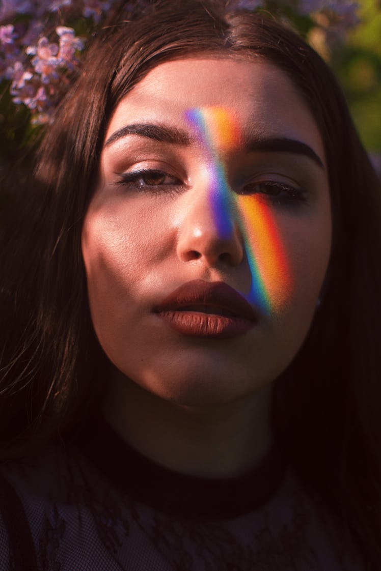 young woman poses around flowers as a rainbow dances across her face, reflects on the 2022 spring eq...