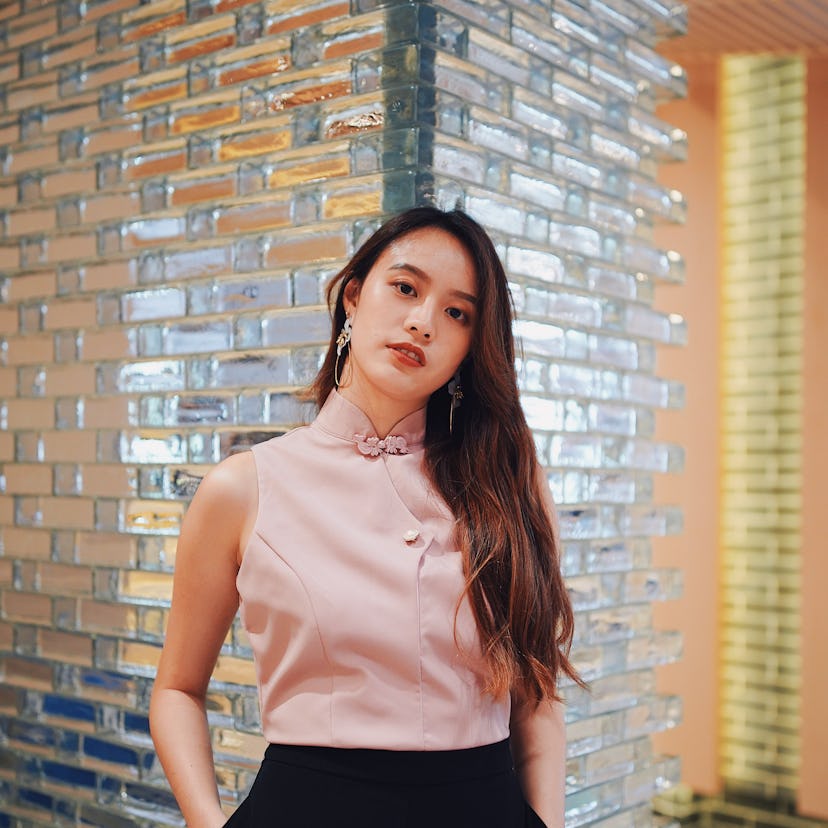 Young woman standing beside a wall of tiles, pondering her zodiac sign's horoscope for the week of M...