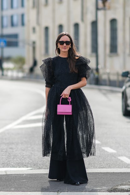 MILAN, ITALY - FEBRUARY 24: A guest wears black sunglasses, gold earrings, a black transparent cut-o...