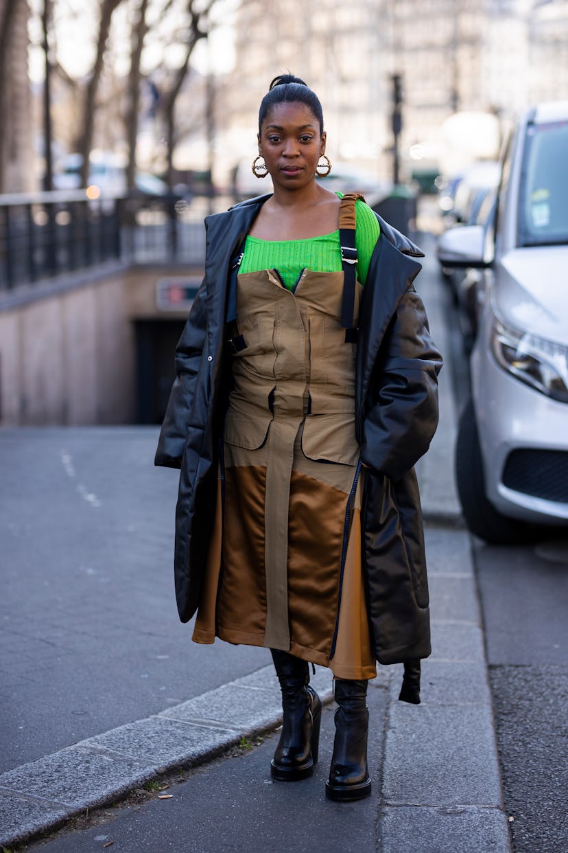 PARIS, FRANCE - MARCH 07: A guest wearing a green top, brown dress, black leather coat and black boo...