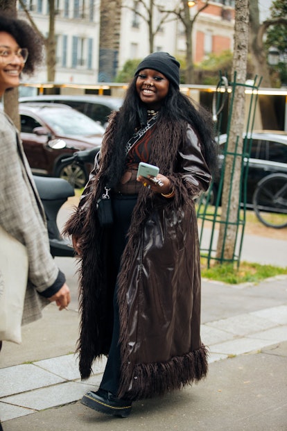 PARIS, FRANCE - MARCH 03: A guest wears a black beanie, ong brown patent leather coat with fur linin...