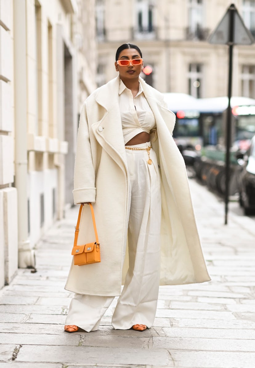 PARIS, FRANCE - MARCH 03: A guest is seen wearing a cream coat, white top and pants with an orange b...