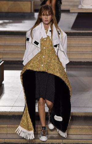 a model wearing a gold peplum dress and white sports jacket on the Louis Vuitton runway