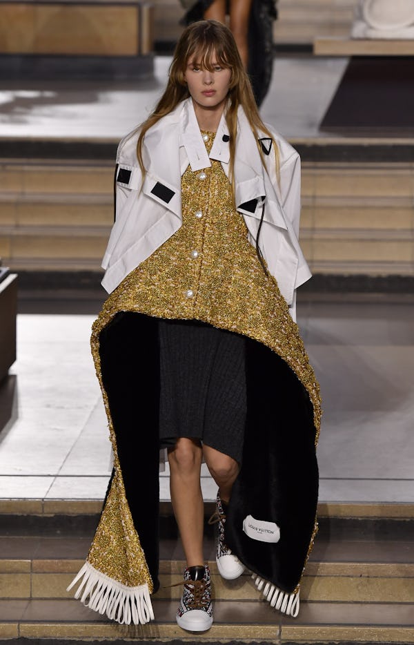 a model wearing a gold peplum dress and white sports jacket on the Louis Vuitton runway