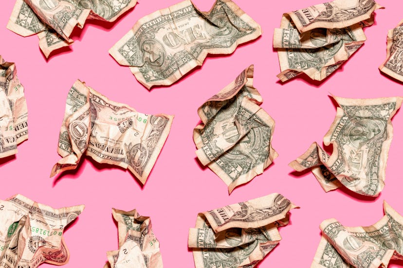 Crumpled up dollar bills on a pink surface due to money fights with friends and family