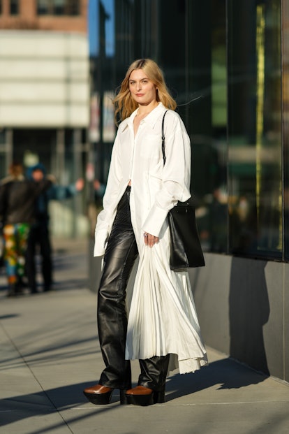 NEW YORK, NEW YORK - FEBRUARY 15: A guest wears a white oversized long shirt, a black shiny leather ...