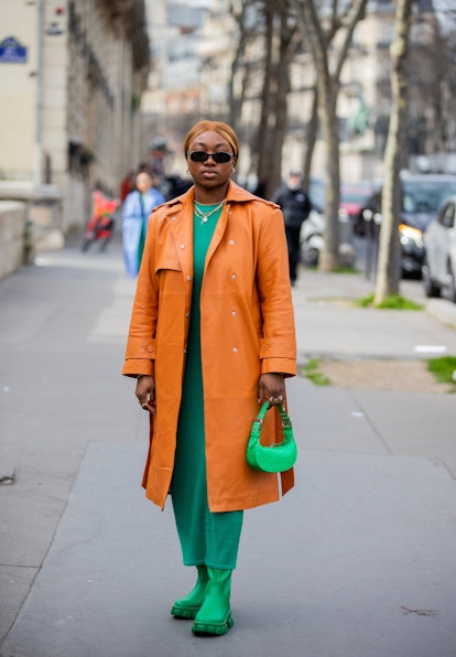 PARIS, FRANCE - MARCH 02: A guest is seen wearing orange suede coat, green dress, bag, boots outside...