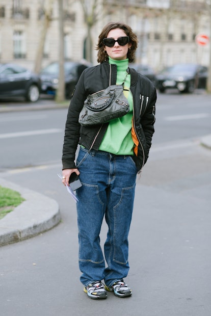 PARIS, FRANCE - MARCH 02: A guest poses wearing a bomber jacket, Balenciaga bag, Carhartt pants and ...