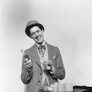 1930s SMILING BARKER IN CHECKERED SUIT WITH MONEY IN HAND POINTING TO BOTTLE OF TONIC LOOKING AT CAM...