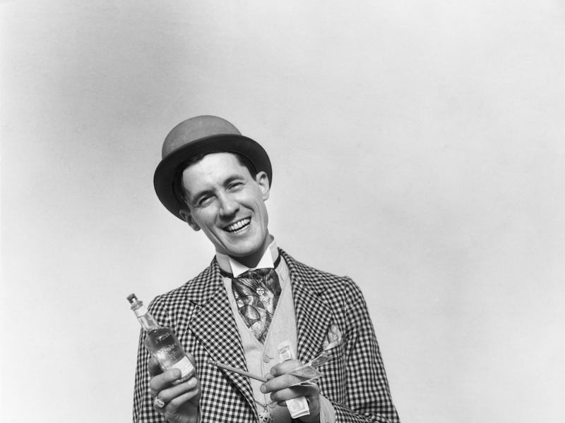 1930s SMILING BARKER IN CHECKERED SUIT WITH MONEY IN HAND POINTING TO BOTTLE OF TONIC LOOKING AT CAM...