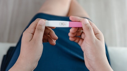 woman looking down at pregnancy test, can you get pregnant a week before your period?