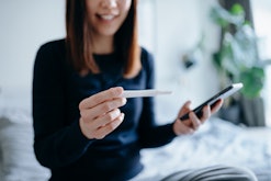 young woman looking at pregnancy test and period tracker app