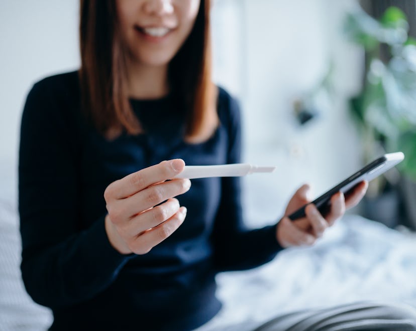 young woman looking at pregnancy test and period tracker app wondering if you can get pregnant a wee...