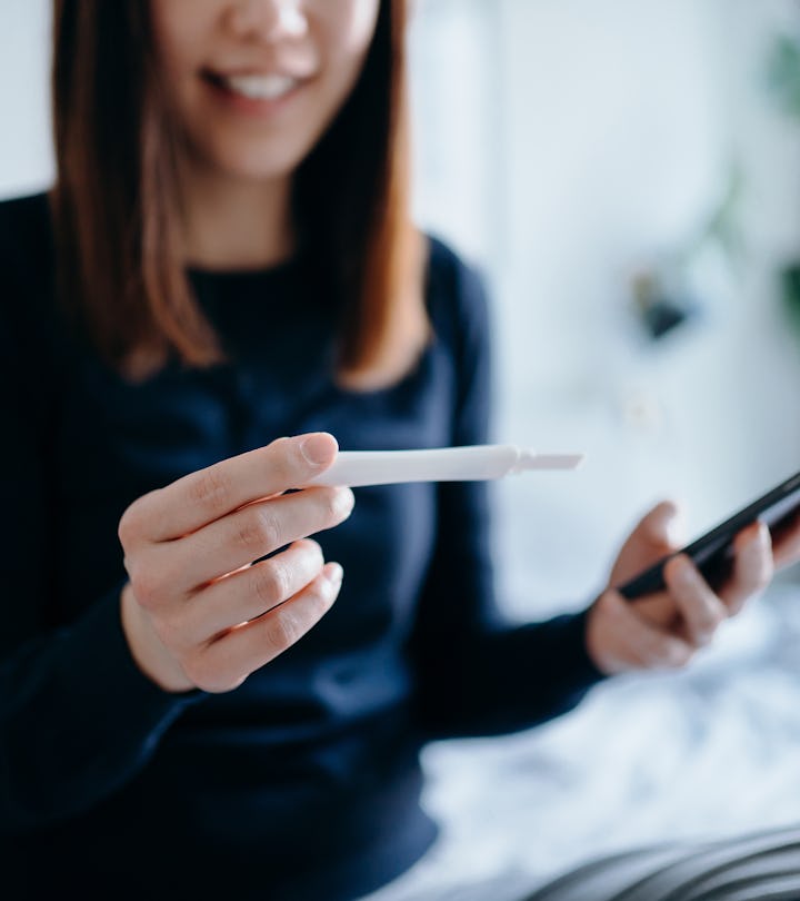 young woman looking at pregnancy test and period tracker app wondering if you can get pregnant a wee...