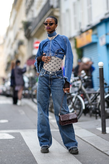 PARIS, FRANCE - MARCH 05: A guest wears brown vintage sunglasses, gold earrings, a blue denim ripped...