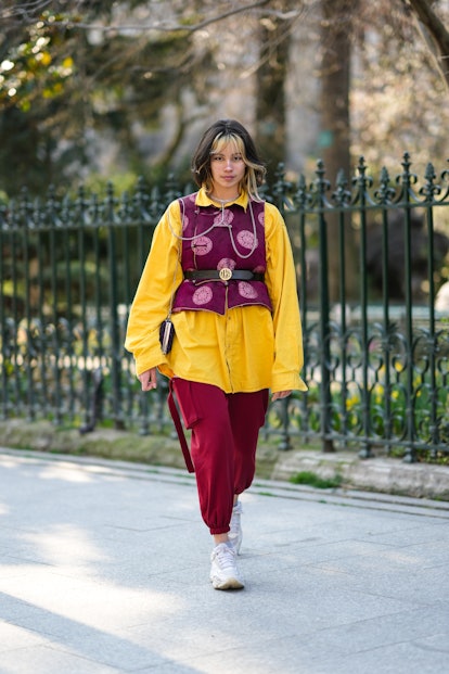 PARIS, FRANCE - MARCH 06: A guest wears a silver long necklace, a yellow oversized shirt, a burgundy...
