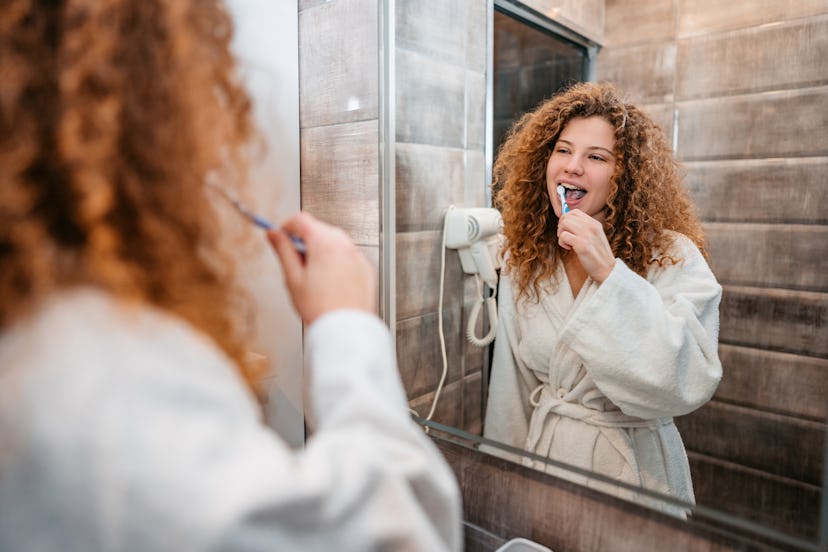 Beautiful young woman brushing her teeth in the bathroom mirror in the morning.