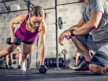 Male fitness coach overseeing his female client while she is doing dumbbell push ups.
