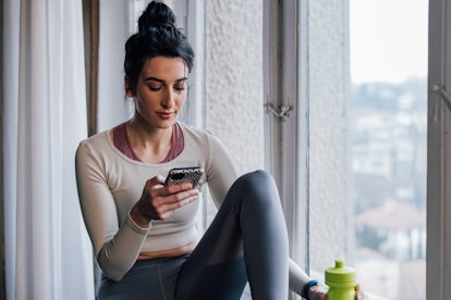 Fit brunette woman sitting next to a window, texting on her mobile phone (horizontal)