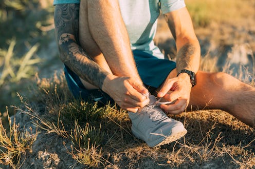 An anonymous white runner tying his shoelace while running in the meadow.