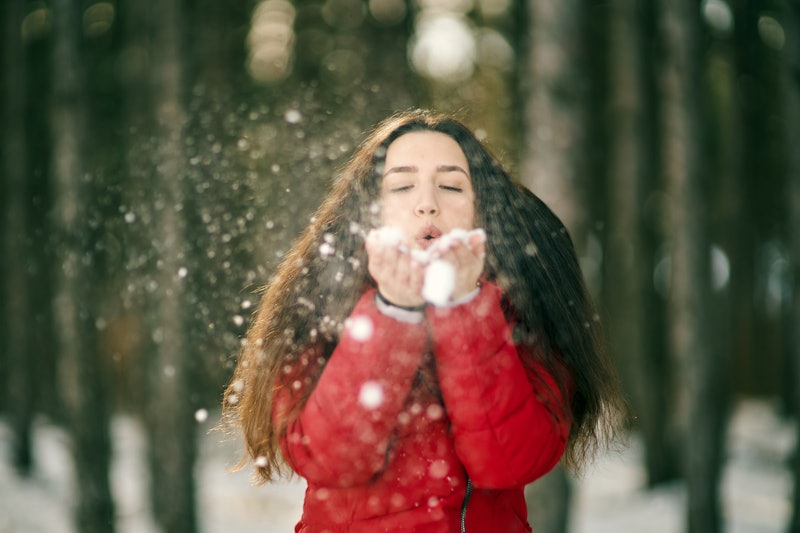 Young woman blowing snow from her hands, having fun in the snow forest. 
Snow forest on background. ...