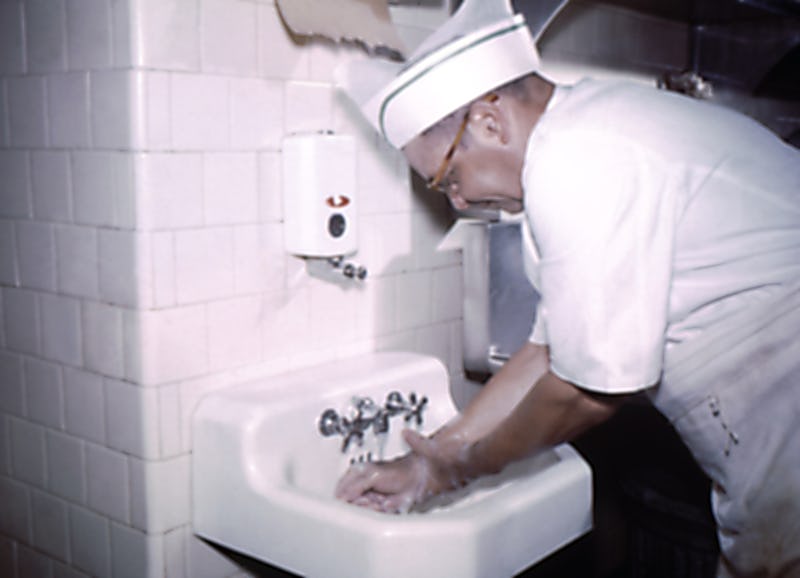 Photograph of a chef in uniform, washing his hands prior to preparing food at a migrant labor work c...