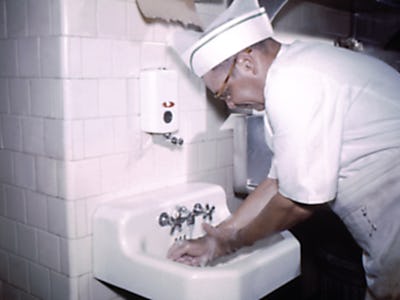 Photograph of a chef in uniform, washing his hands prior to preparing food at a migrant labor work c...