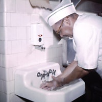 Photograph of a chef in uniform, washing his hands prior to preparing food at a migrant labor work c...
