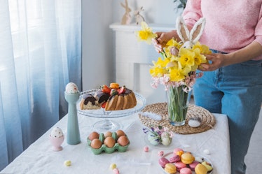 Woman decorating Easter table with a sweet Easter bunny and spring flower bouquet.