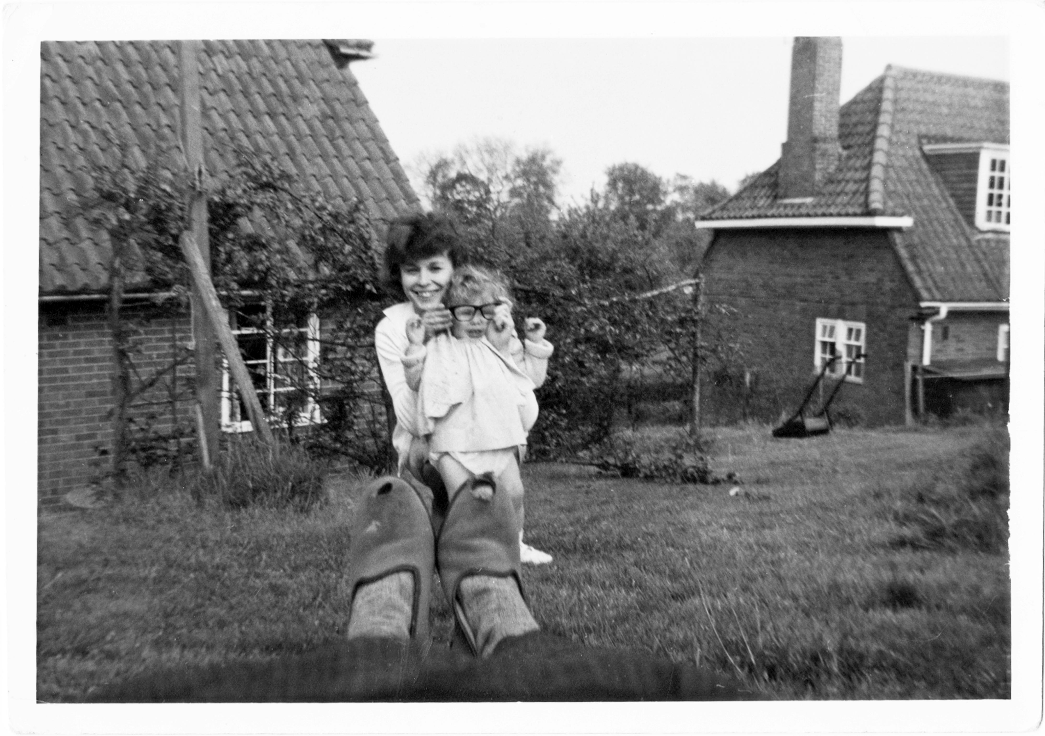 Woman putting pair of dark rimmed glasses on  toddler with pair of tatty slippers in foreground.