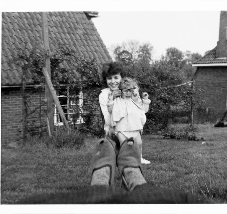 Woman putting pair of dark rimmed glasses on toddler with pair of tatty slippers in foreground.
