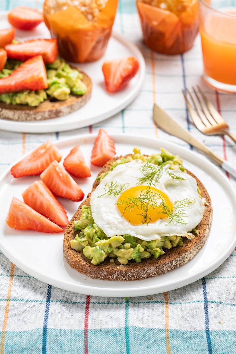 Avocado toast topped with a sunny-side-up egg with sliced strawberries for garnish, a perfect meal f...
