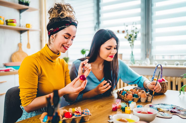 Two beautiful girlfriends painting eggs together for Easter