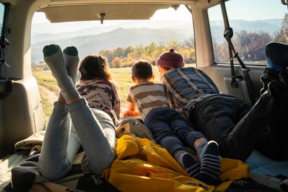 A small family lying on their tummies and looking out of the trunk of a mini van at a rural scene