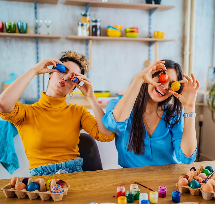 Two women hold up Easter eggs and plan Easter games for kids and adults.