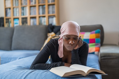 A middle aged woman wearing a head scarf reads a book on the couch.
