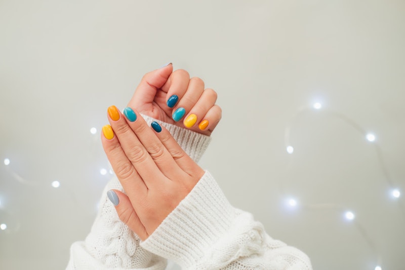 Trendy bright manicure on woman hands in white knitted sweater against ultimate gray background with...