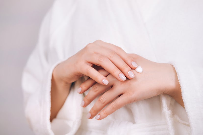 Woman in white bathrobe with nude pink manicure rub natural organic cream in hand's skin to moisturi...