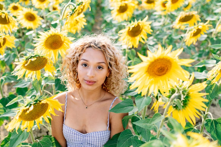 Young woman with curly hair standing in a sunflower field, knowing her lucky zodiac sign will have t...